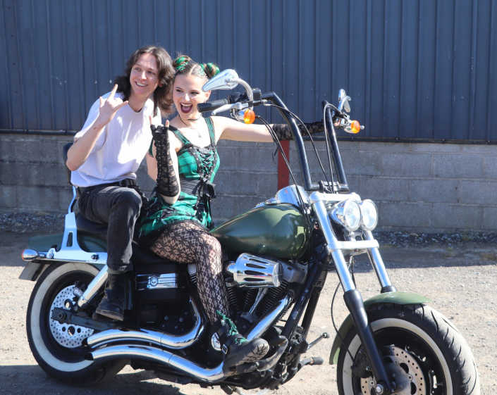 the cast of "We Will Rock You" in costume for a promotional photo-shoot. "Scaramouche" is riding a motorbike with "Galileo" riding pilion.